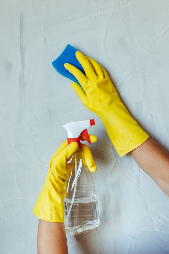 services-04 Hands in yellow gloves cleaning wall with sponge and spray bottle.