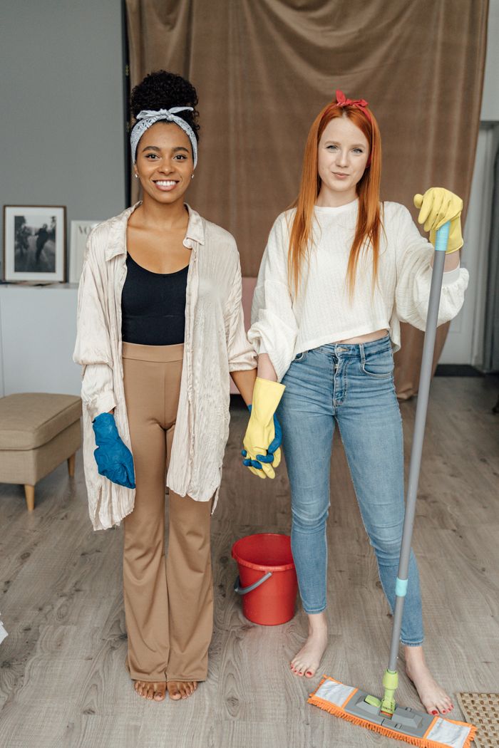 journey Two women smiling and holding hands while cleaning indoors, symbolizing teamwork.