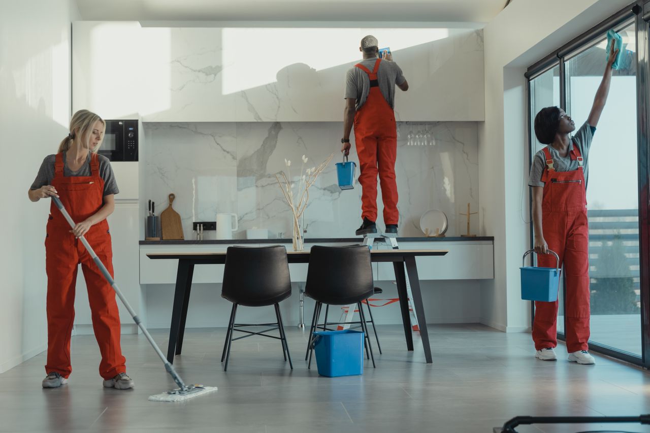 team-03 Group of cleaners in red uniforms mopping and wiping glass in a modern dining room.